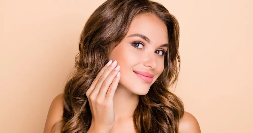 Woman showing smooth, glowing skin smiling and touching her cheek after receiving Dermal Fillers in Reno, NV