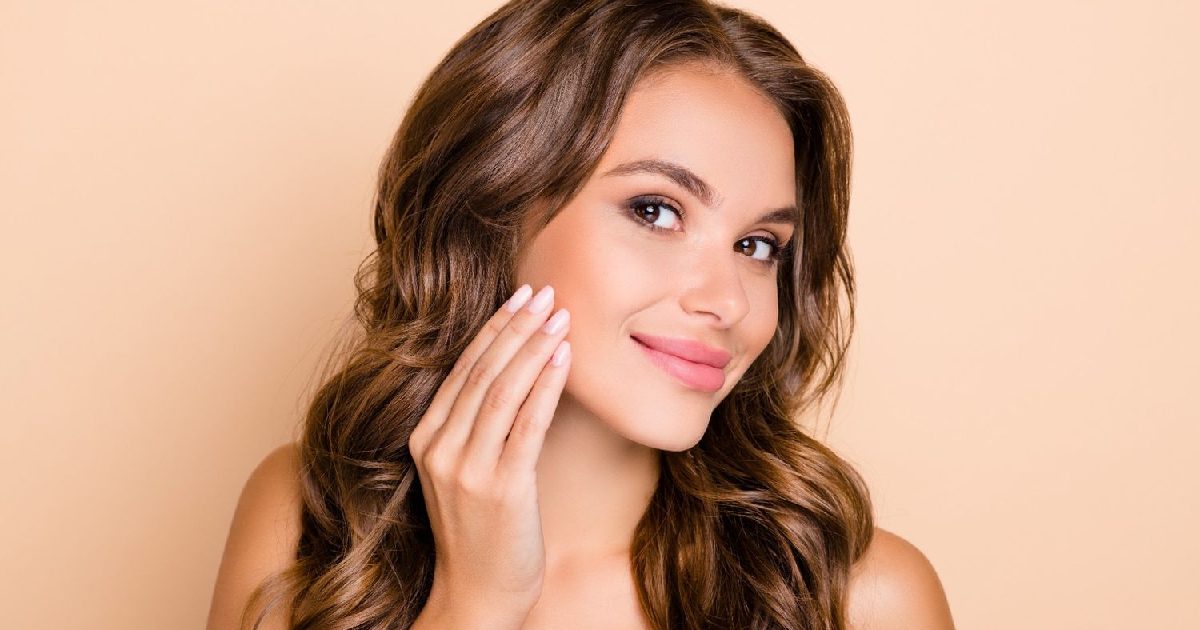 Woman showing smooth, glowing skin smiling and touching her cheek after receiving Dermal Fillers in Reno, NV